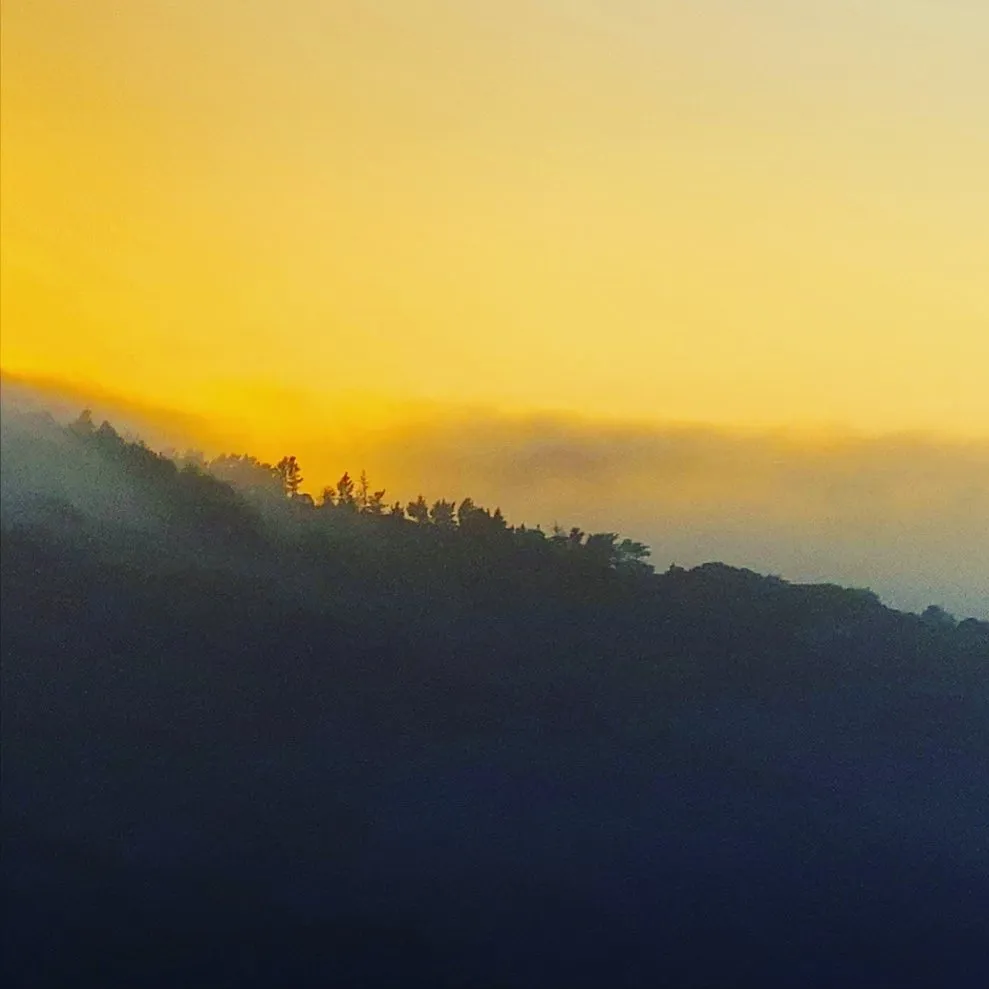 A dark, silhouetted ridge line spans the bottom third of the frame against a warm gradient sky of yellow and orange, separated by a soft layer of mist.