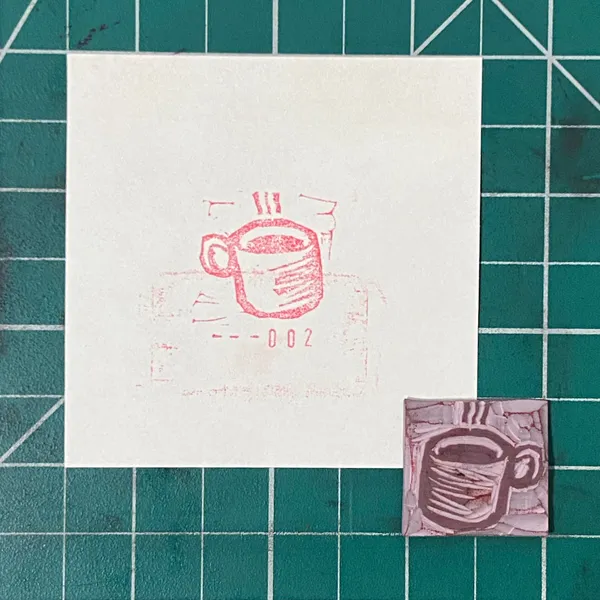 The composition features a white sheet on a teal grid, displaying a red outline drawing of a mug and the number --002, next to a smaller purple square with a dark gray outline drawing of a mug.