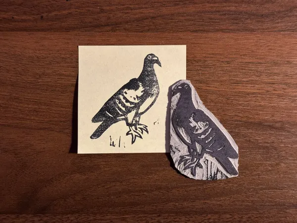 On a dark wood background, two black and white prints of birds are displayed: one on a square cream card showing a bird facing right, and another on an irregular white card showing a bird facing left.