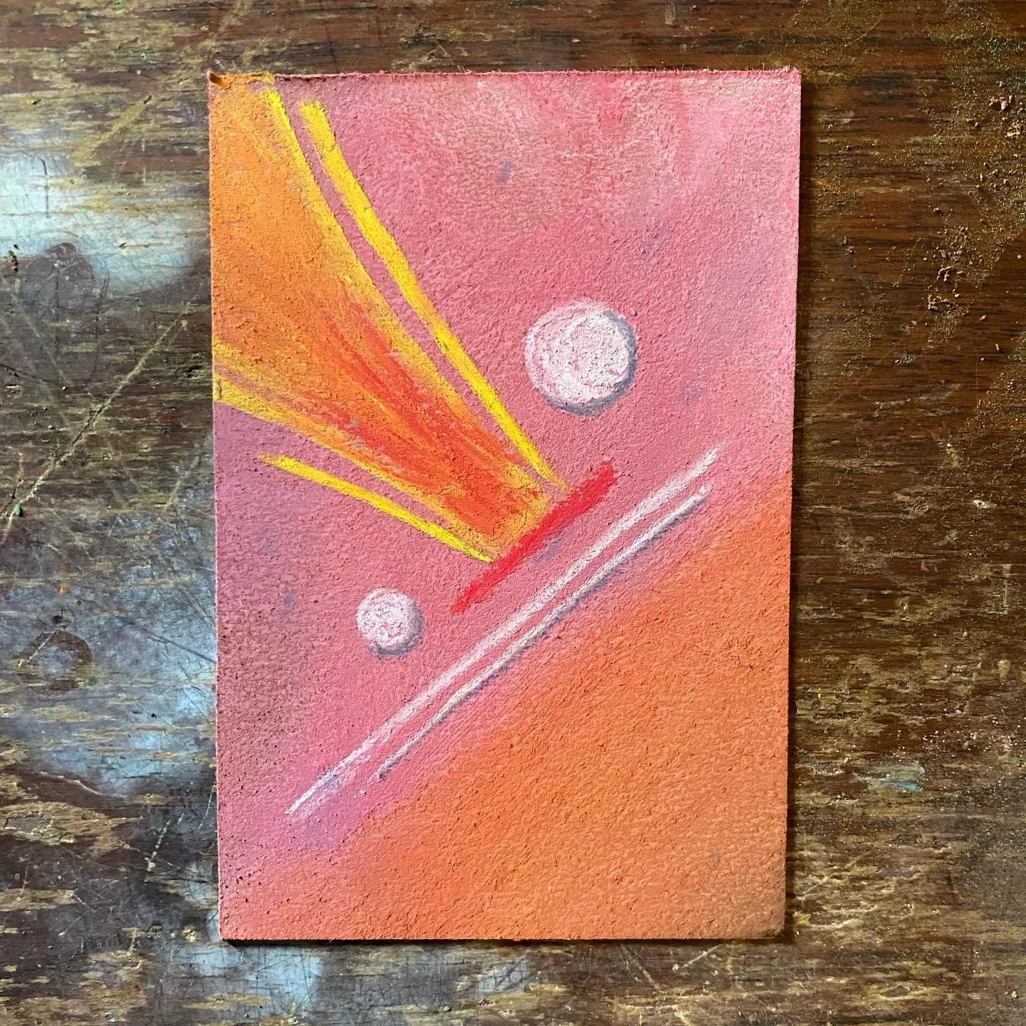 A rectangular artwork shows a gradient sky of pink and orange, featuring a radiating yellow and orange sunburst on the left, two white circles, and diagonal white and red streaks across the lower half.