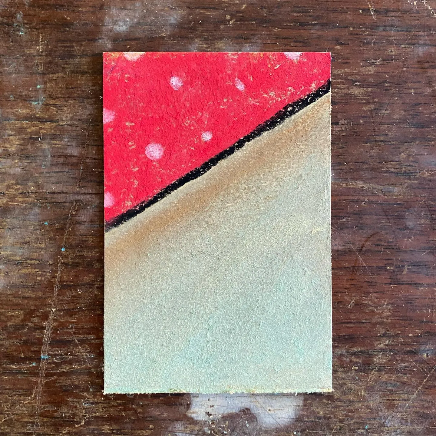 A vertical artwork featuring a red upper section with white spots, separated by a jagged black line from a smooth, light beige lower section.