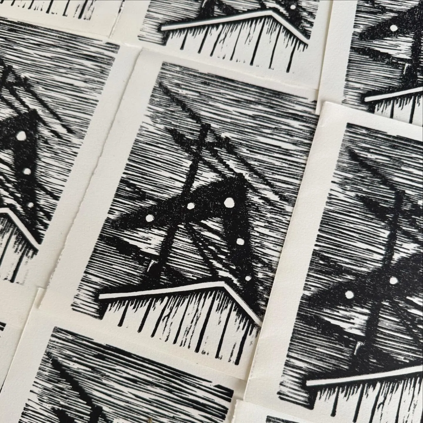 Multiple rectangular prints display a repeating motif of a house silhouette over a highly textured field of dense black diagonal lines, triangles, and dots.