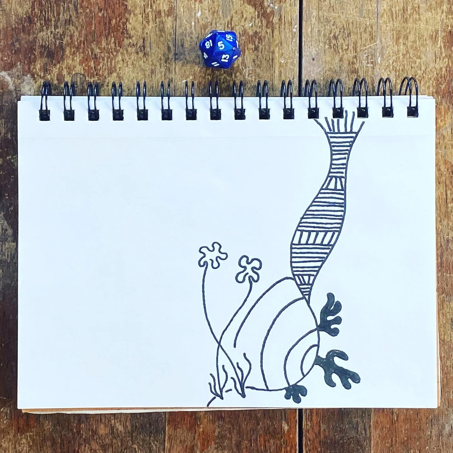 Black ink drawing of a stylized seahorse with striped body markings, drawn on white paper and positioned on a rustic wooden surface.