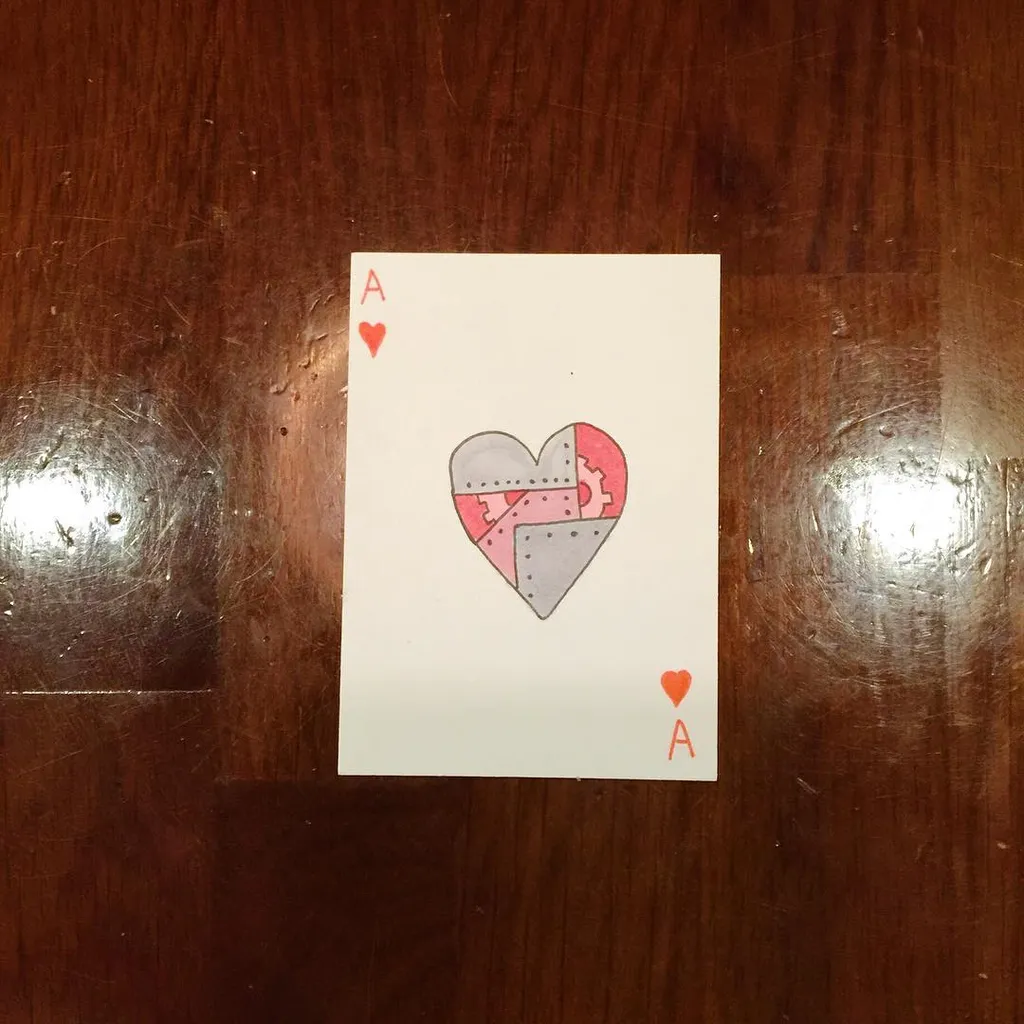 The card rests on dark wood grain, featuring the Ace of Hearts and a central drawing of a heart composed of three interlocking puzzle pieces in red and gray tones.
