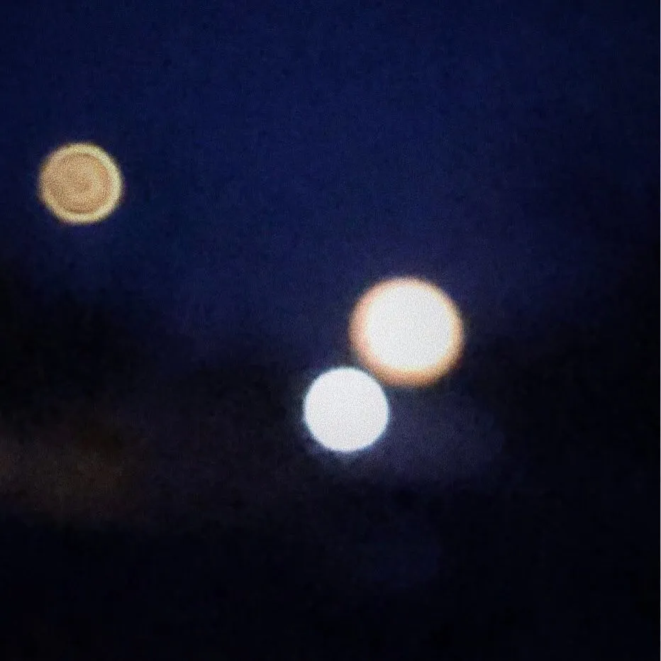 Against a dark navy background, several blurred, glowing orbs of yellow, orange, and white light are visible, creating a bokeh effect.