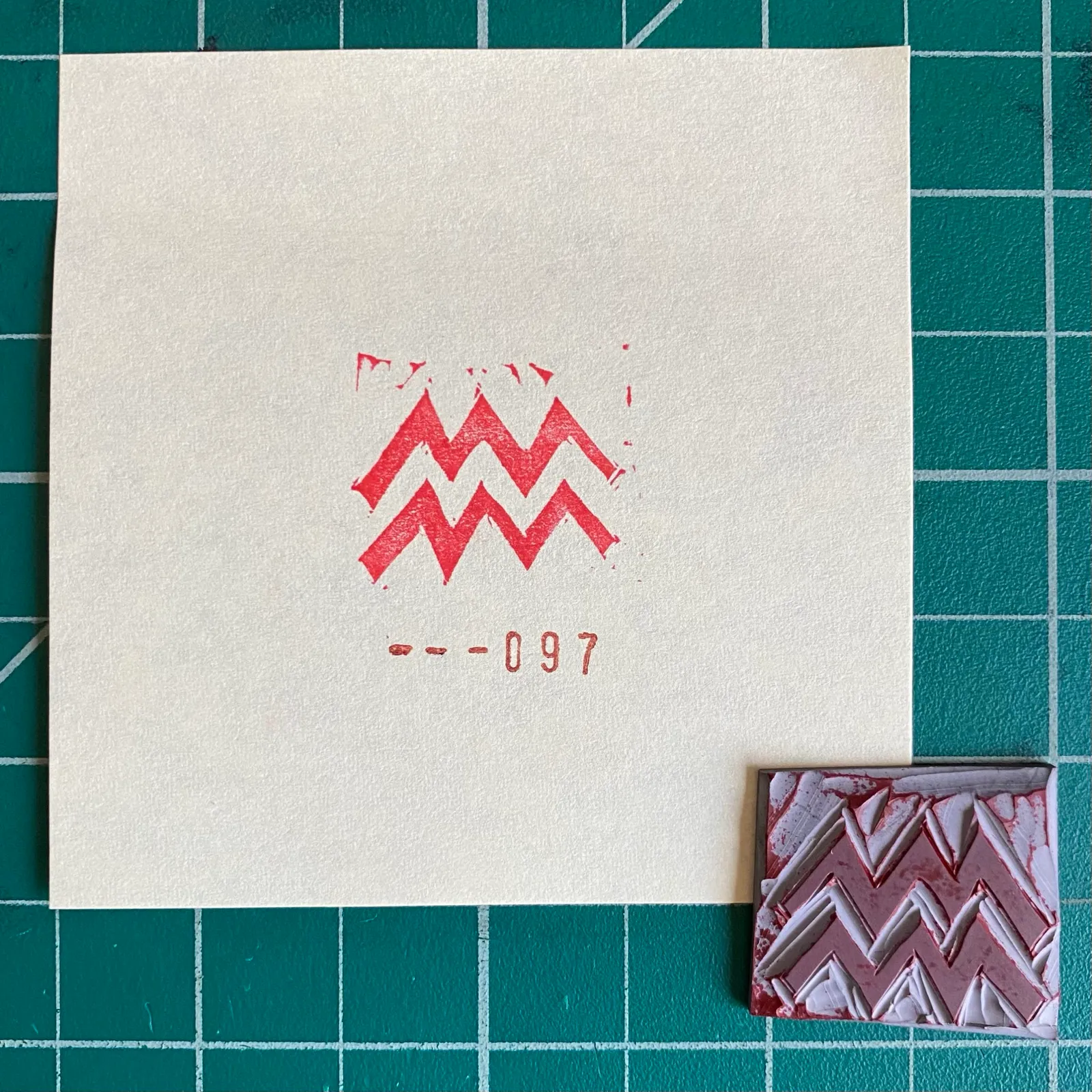 A cream card on a teal grid displays a red zigzag motif and the number --097, positioned next to a small rectangular sample featuring layered red and white zigzags.