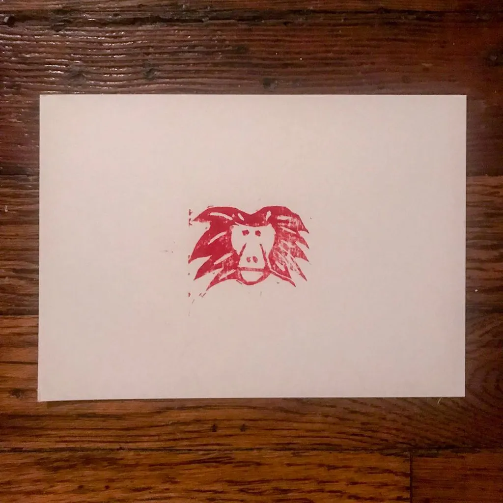 Centered on a cream background is a rough, red drawing of a stylized face with prominent features and wild, spiky hair, executed in a distressed, stamped style.