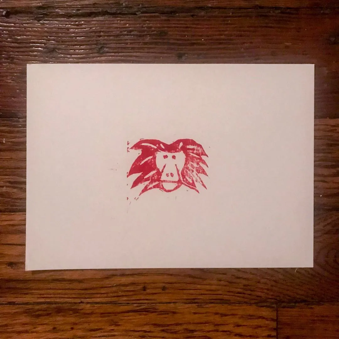 Centered on a cream background is a rough, red drawing of a stylized face with prominent features and wild, spiky hair, executed in a distressed, stamped style.