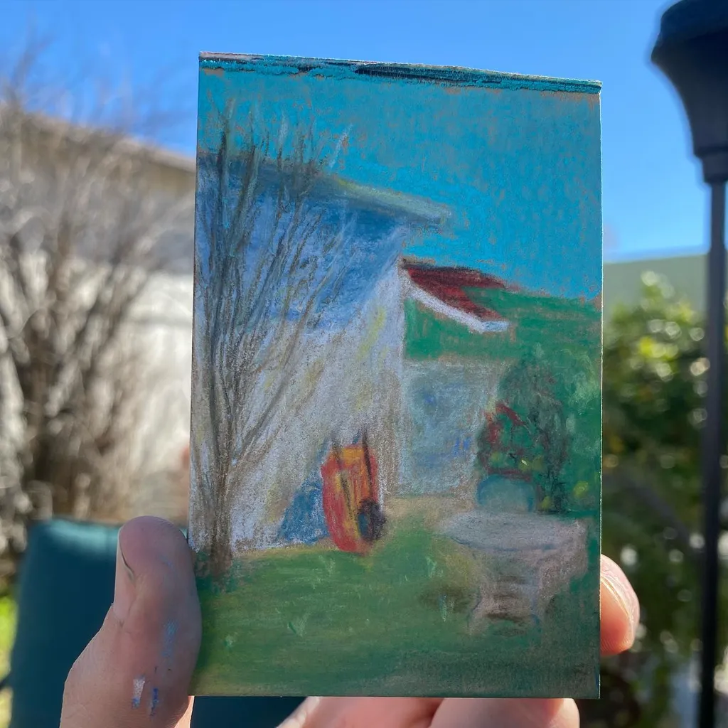 A painting depicts a house under a bright blue sky, featuring a bare tree on the left, green foreground grass, and a small patio area with visible brushstrokes.
