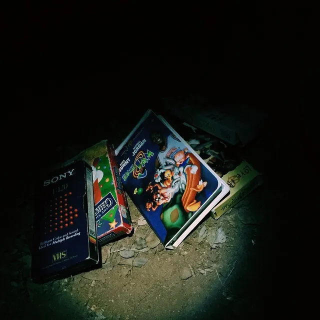 Several colorful VHS tapes are grouped on a rough, dark surface, with the bright covers contrasting sharply against the deep shadows.
