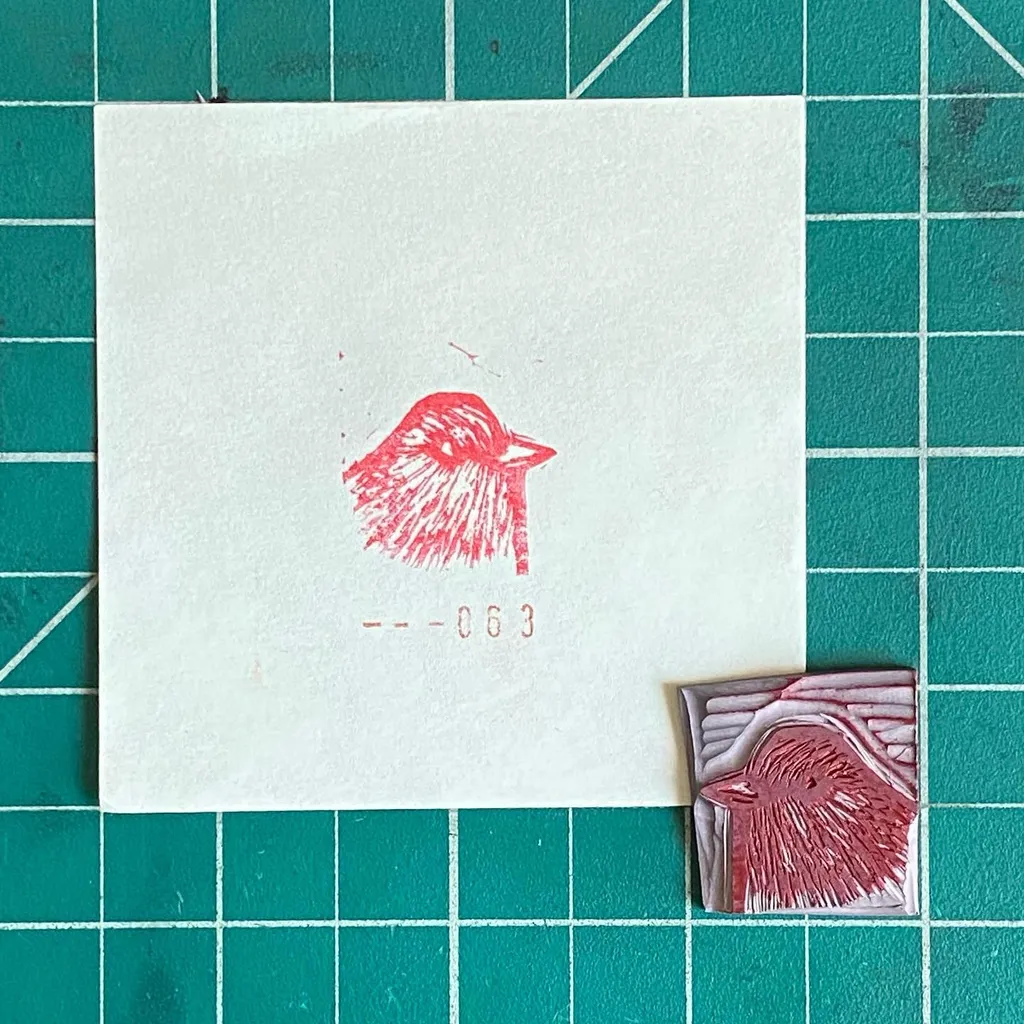 A white square paper on a green grid features a red, textured drawing of a bird and the numbers 063, next to a small, rectangular piece of red and white textured art.