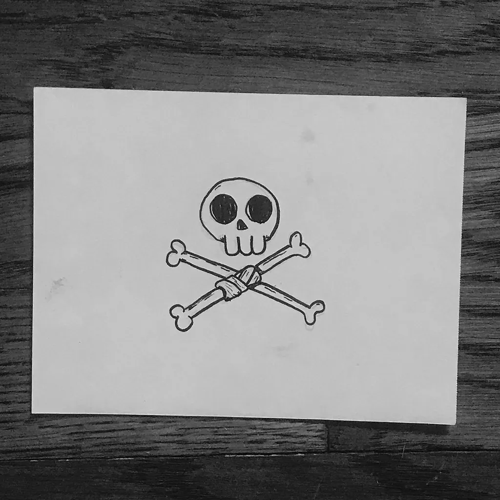Simple black line art depicts a skull and two crossed bones, drawn on white paper set against a dark wood background.