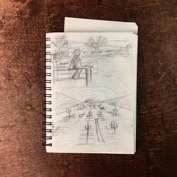 A sketchbook filled with graphite sketches of outdoor scenes, featuring a seated figure and a landscape composition with a prominent central circle, rests on a dark brown surface.
