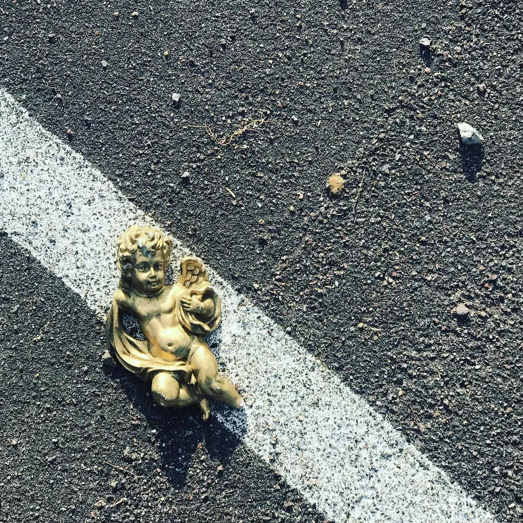 A small bronze cherub statue rests on dark asphalt marked by a thick, bright white painted line.