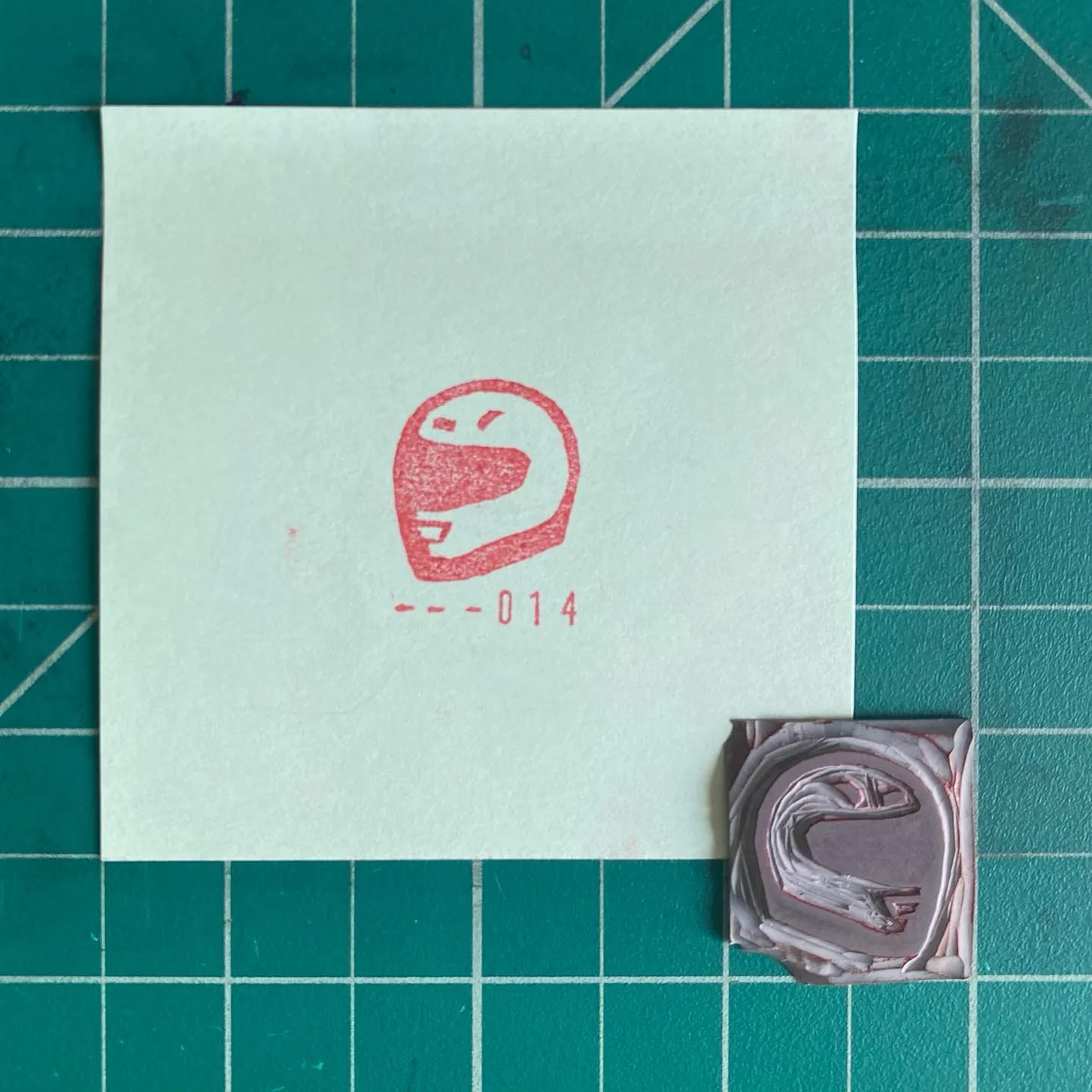 A white card featuring a red, stylized smiling face and the text --014 is positioned on a teal grid background, next to two small, layered squares of brown and gray tones.