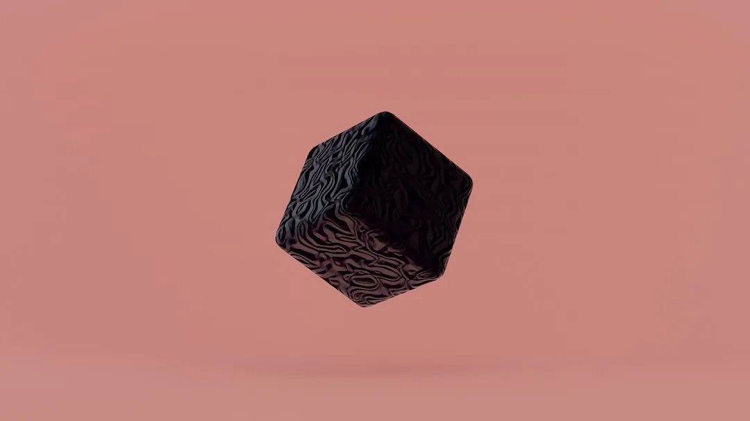 A dark, textured cube floats against a solid pale pink background, featuring intricate, raised, organic patterns across its visible faces.