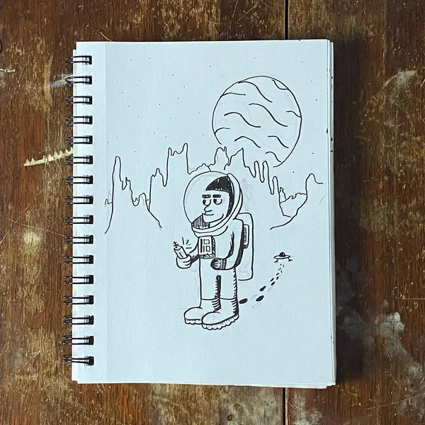 A line drawing on white paper depicts a cartoon astronaut standing before jagged mountains and a large circular planet.