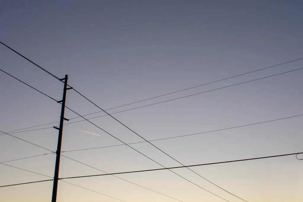 A dark utility pole anchors the left side, while multiple thin wires traverse a sky gradienting from deep slate blue overhead to pale yellow near the horizon.