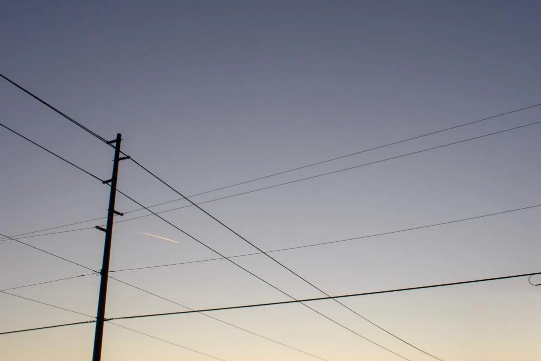 A dark utility pole anchors the left side, while multiple thin wires traverse a sky gradienting from deep slate blue overhead to pale yellow near the horizon.