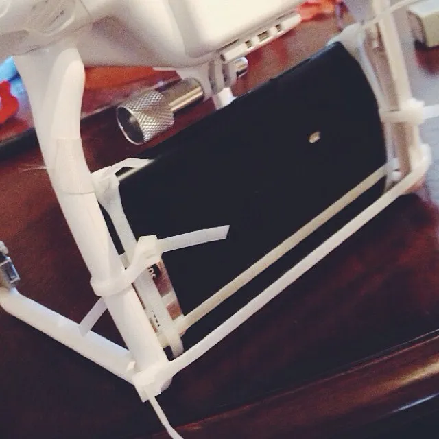 A black smartphone is held by a white, adjustable mount on a dark, polished wooden surface, contrasting the matte white structure with the reflective wood grain.