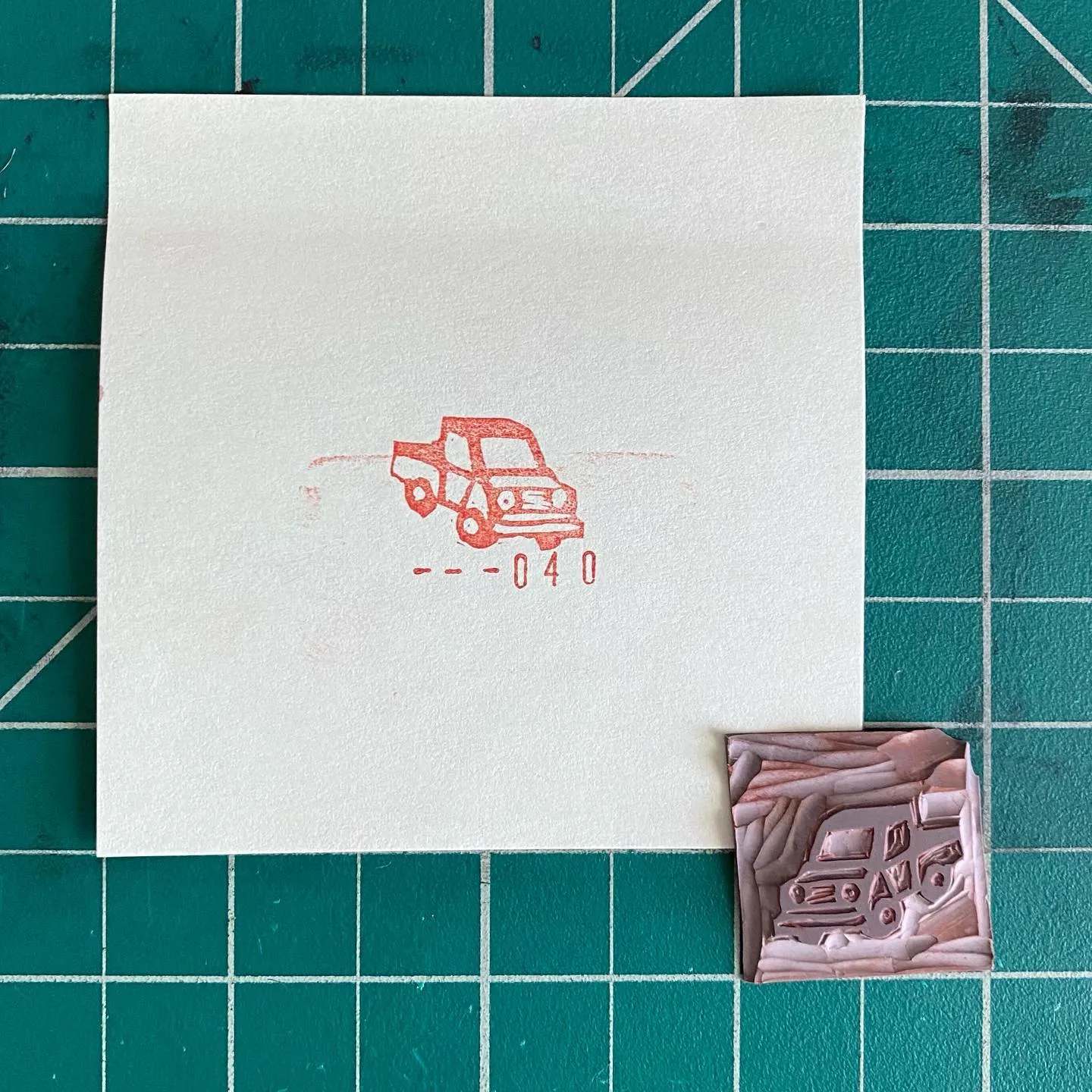 A white square features a red line drawing of a car and the numbers --040 on a teal grid, accompanied by two carved rectangles: one with red lines and the other with intricate brown and gray geometric patterns.