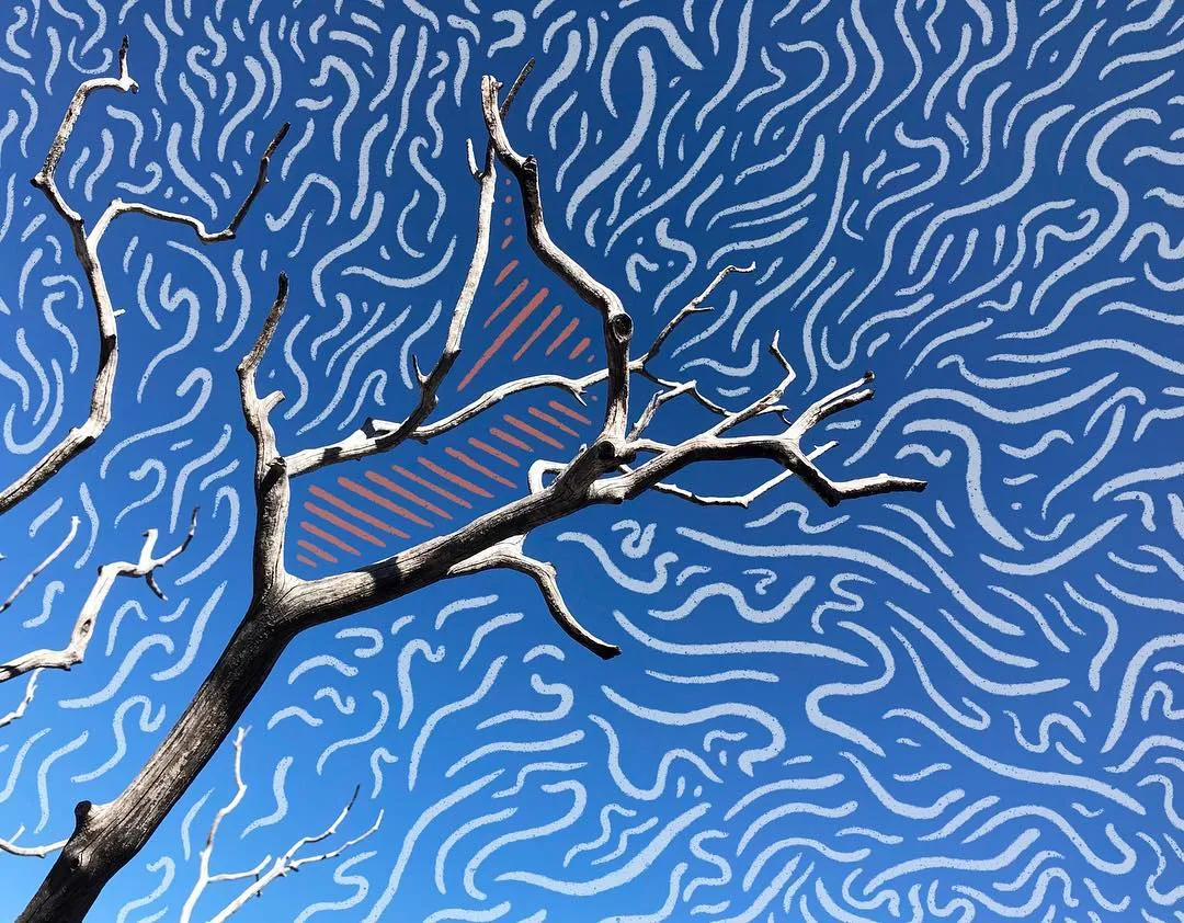 Bare, dark branches are silhouetted against a bright blue background patterned with dense, wavy white lines, framing a central orange geometric shape.