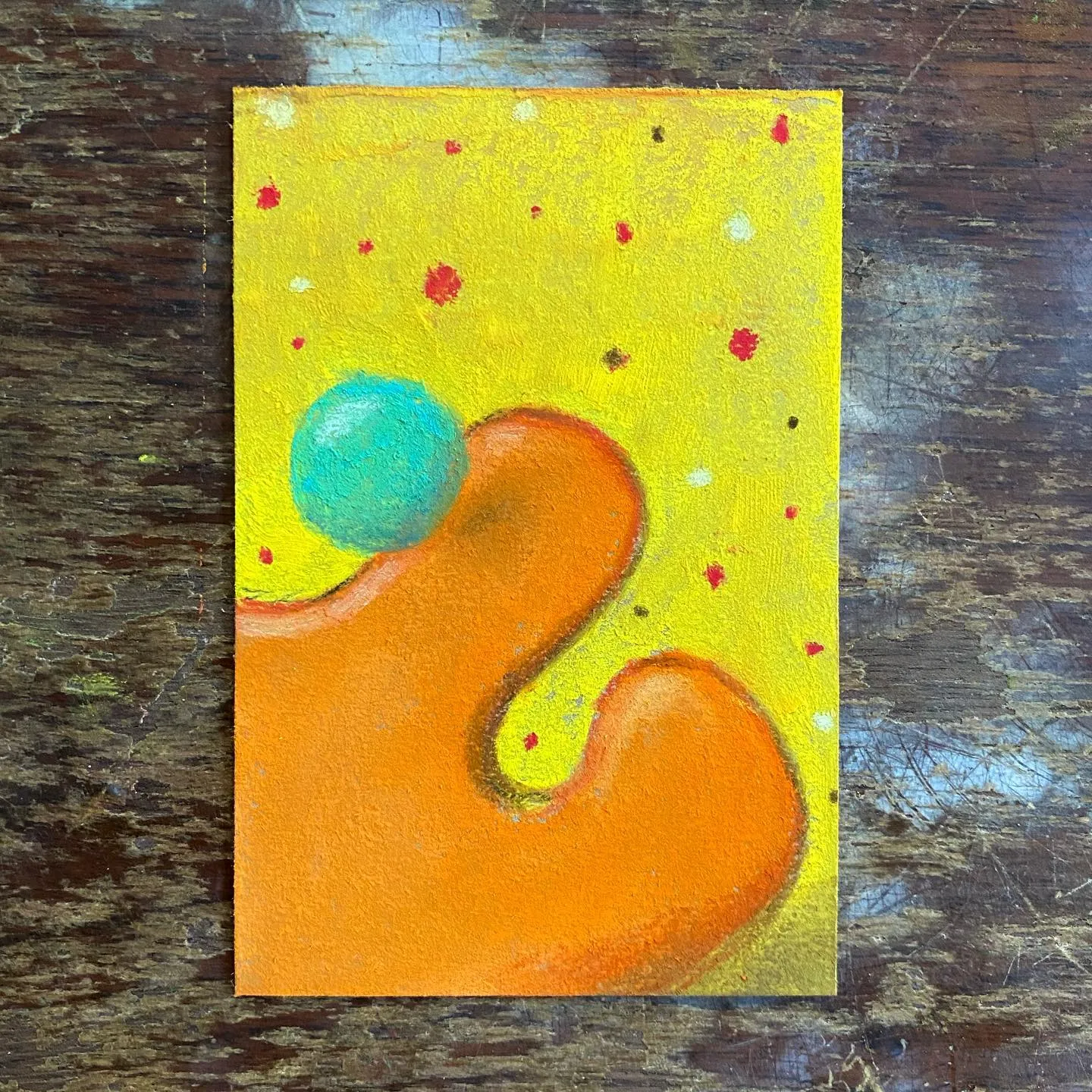 Bright orange, curved figure dominates a yellow background speckled with red and yellow dots, featuring a teal sphere attached to its upper left curve.