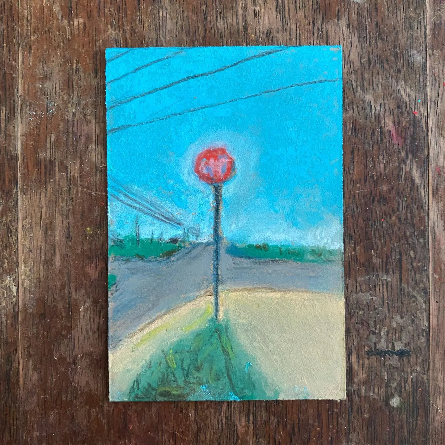 A vertical painting depicts a roadside scene under a bright cyan sky, centered by a large red sphere on a pole, with a muted landscape and tan foreground, all mounted on rough brown wood.