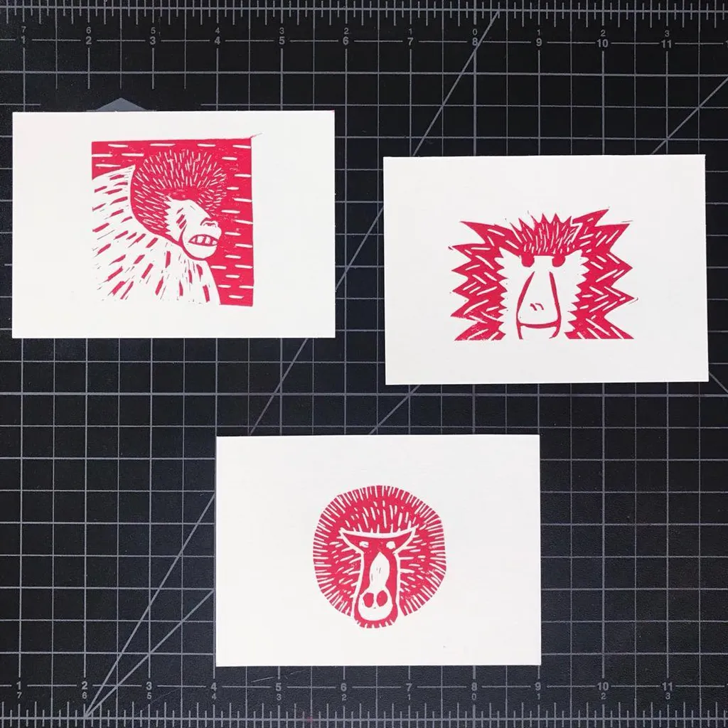 Three stylized red drawings of animal faces are displayed on white paper against a black grid background, featuring varied patterns including hatching, jagged lines, and a central circular design.