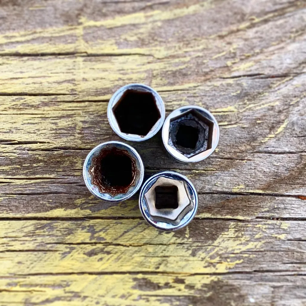 Five metallic hexagonal nuts are arranged on a distressed wooden surface featuring yellow and brown tones, contrasting the shiny hardware against the weathered grain.