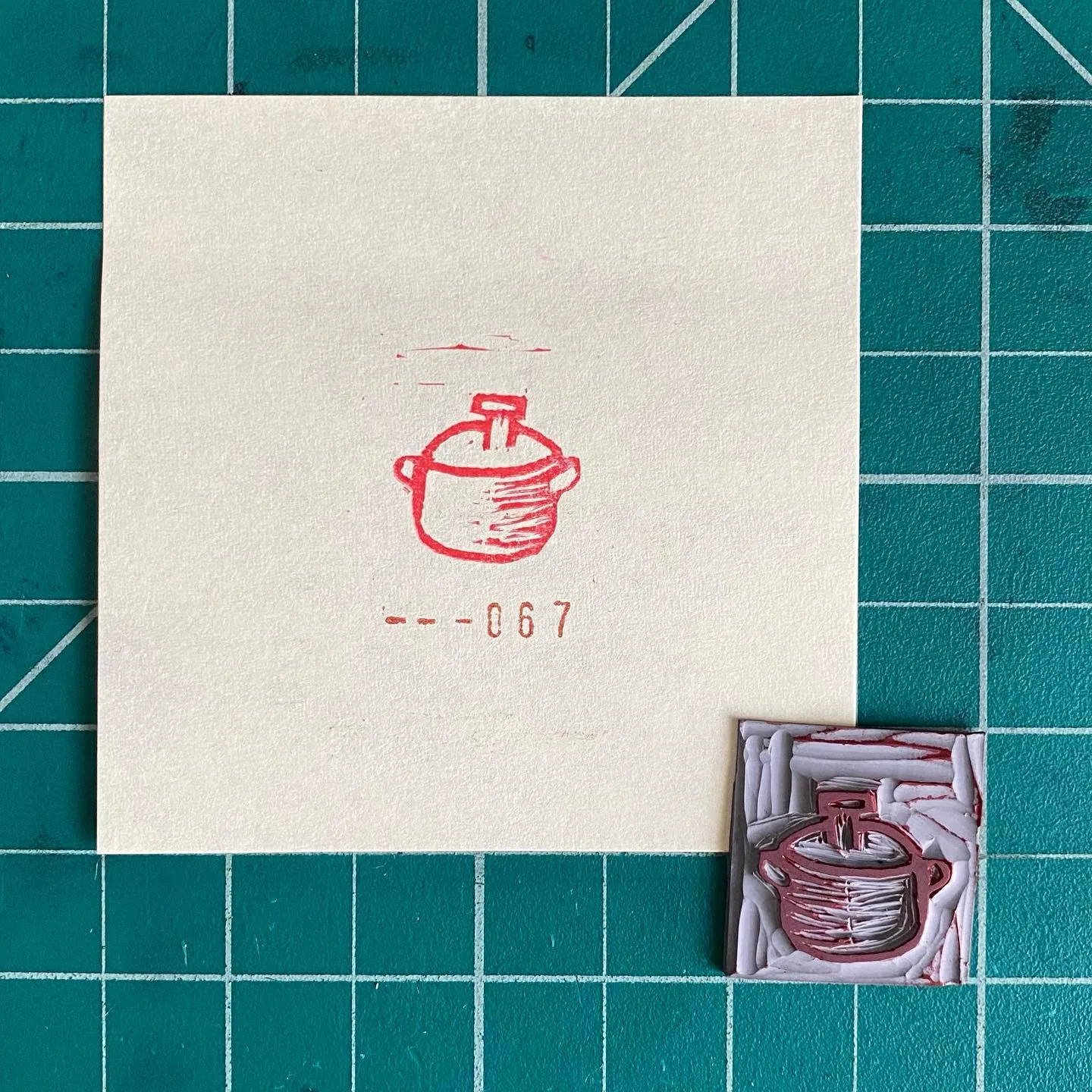 A cream square displays a red line drawing of a pot and the number --067, positioned next to a smaller, textured square featuring a layered red rendering of the same pot.