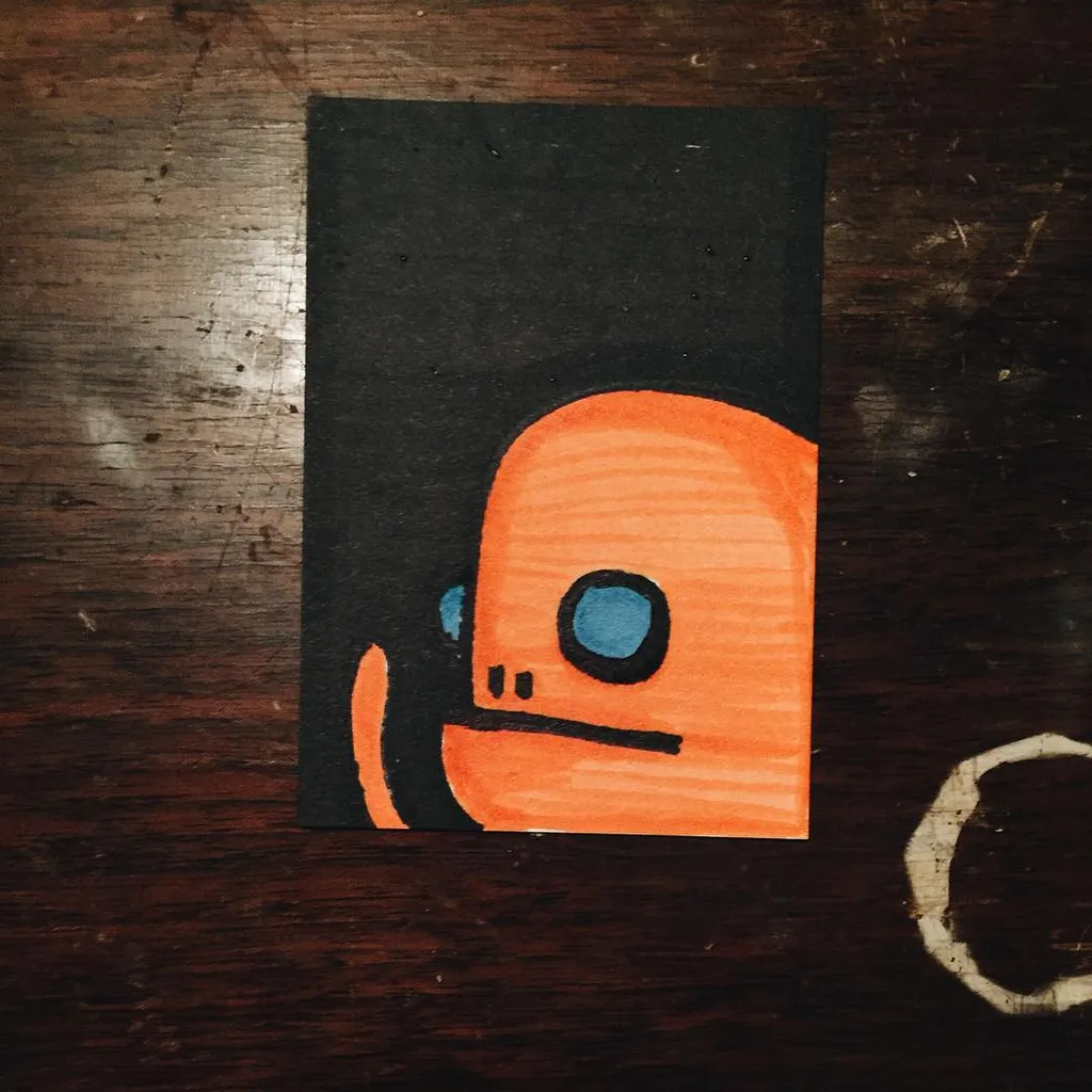 A stylized orange figure with large blue eyes and a small mouth is set against a solid black rectangle, which rests on a dark, wooden surface.