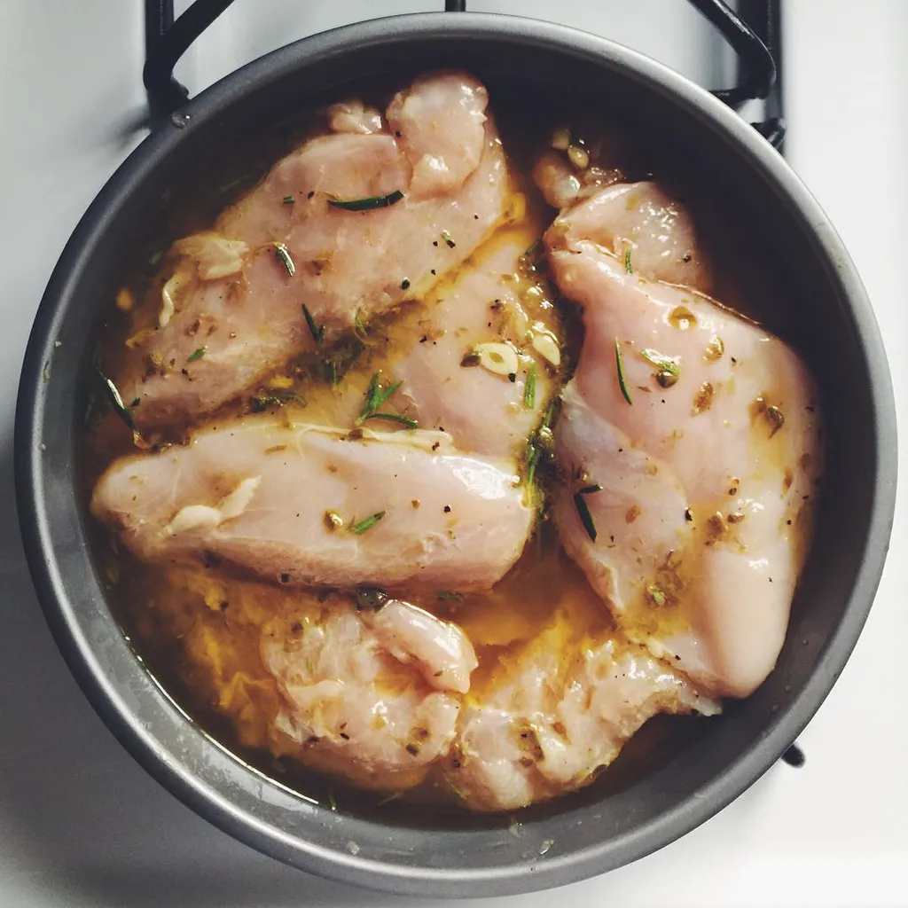 The composition shows several pale chicken pieces resting in a dark pot, submerged in a glossy, golden liquid speckled with green herbs and dark spices.