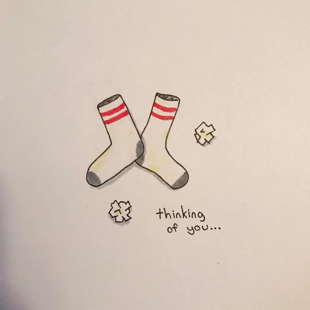 Crossed cartoon socks with red stripes and gray cuffs are drawn on white paper, accompanied by the text thinking of you... and small sock doodles.