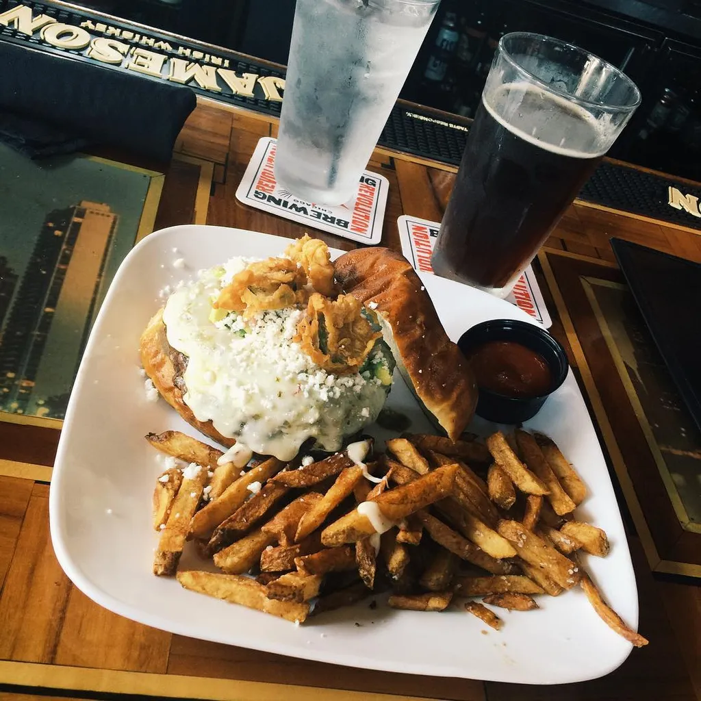 On a white plate, golden french fries surround a breakfast item topped with white sauce, resting on a wooden table near two glasses and dark dipping sauce.