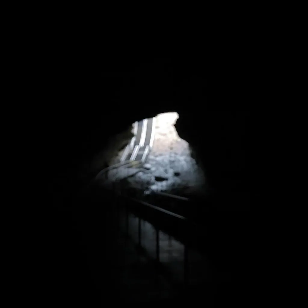 High contrast composition featuring a small, dark opening that reveals a textured surface with vertical white stripes and dark, linear elements below.