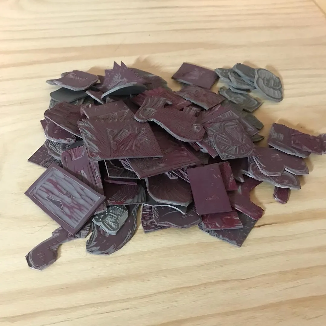 Overlapping, irregularly shaped pieces featuring carved details and patterns, clustered on a light wood surface, displaying colors ranging from deep maroon to slate gray.