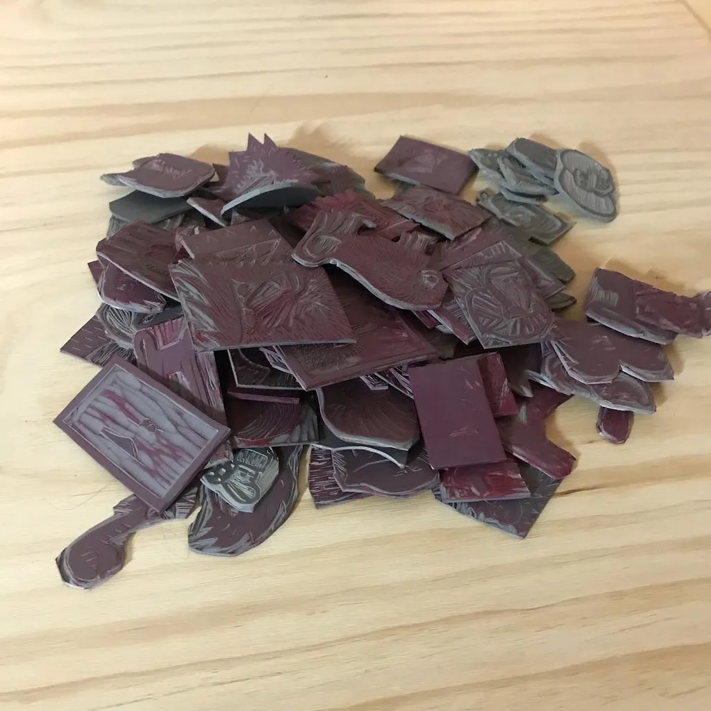 Overlapping, irregularly shaped pieces featuring carved details and patterns, clustered on a light wood surface, displaying colors ranging from deep maroon to slate gray.