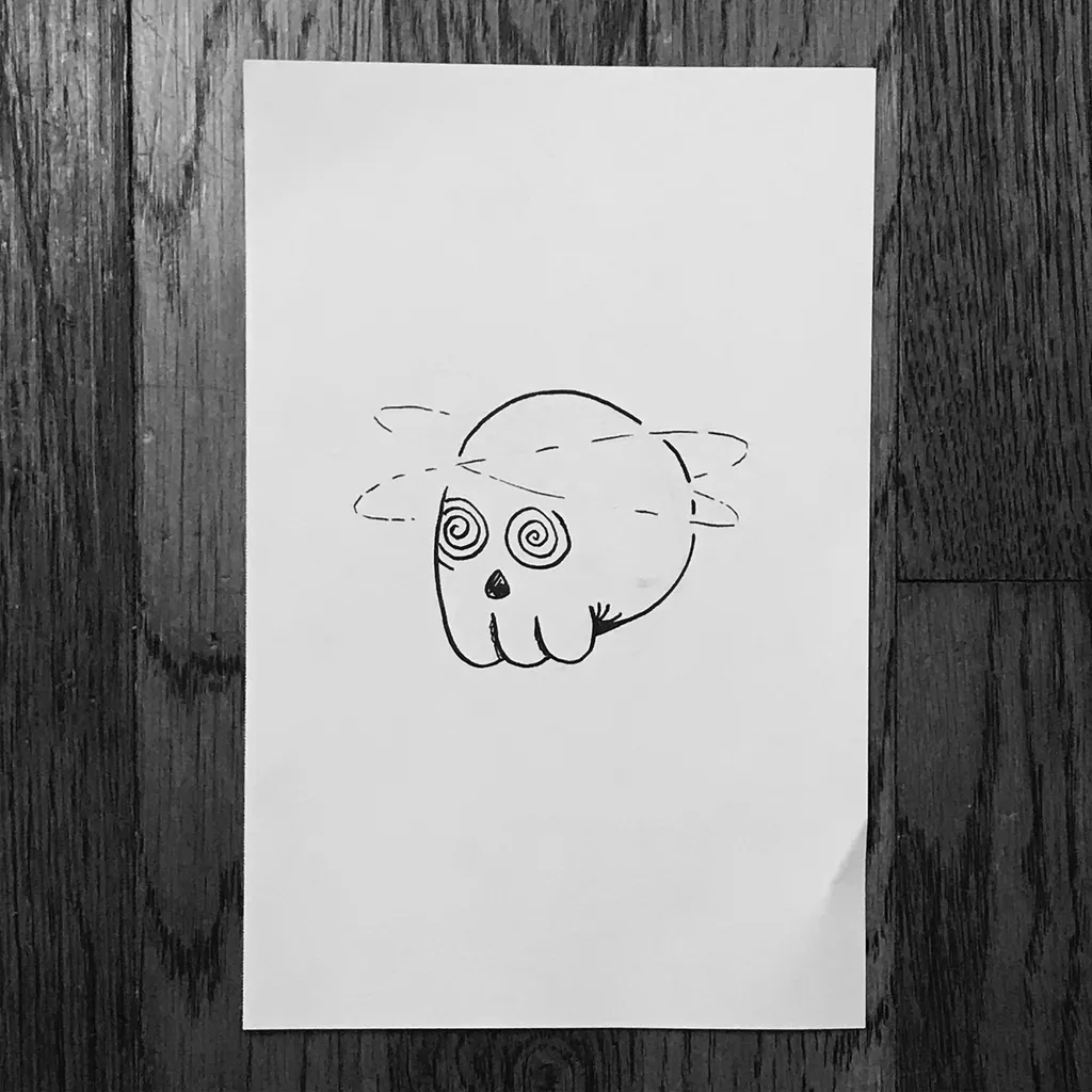 A simple black line drawing of a cartoon owl face with large circular eyes and small feet, centered on white paper against a dark wooden background.
