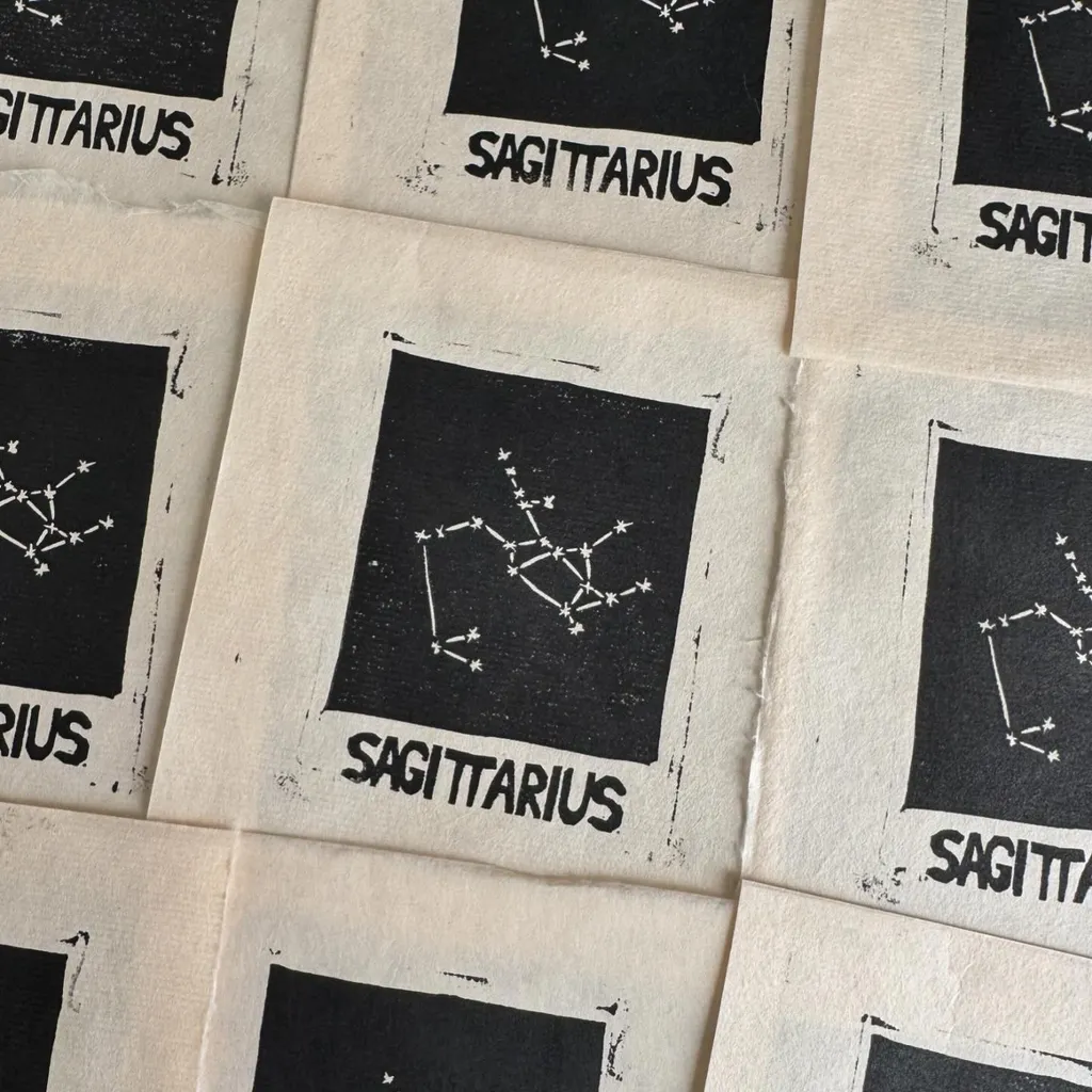 A collection of small, cream-colored prints featuring the black text SAGITTARIUS and a simple black constellation diagram of stars, arranged in a scattered, overlapping pattern.