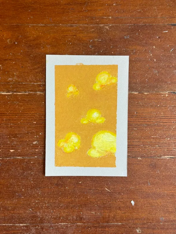 A vertical painting on a mustard yellow background features several scattered, irregular shapes of bright yellow and gold, painted with visible, soft brushstrokes.