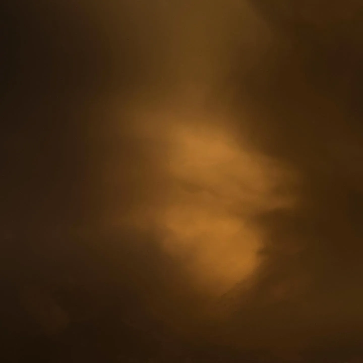 Diffused clouds in deep browns and burnt orange tones fill the frame, with a soft, glowing center that suggests atmospheric depth and texture.