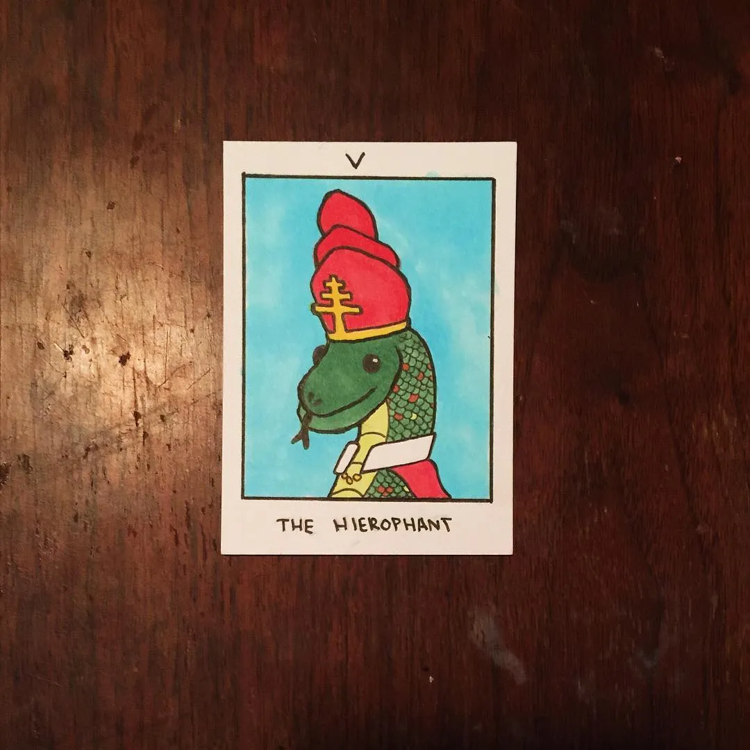 The card features a green snake figure wearing a red and yellow crown and a white garment, set against a light blue background, with the title THE HIEROPHANT printed below.