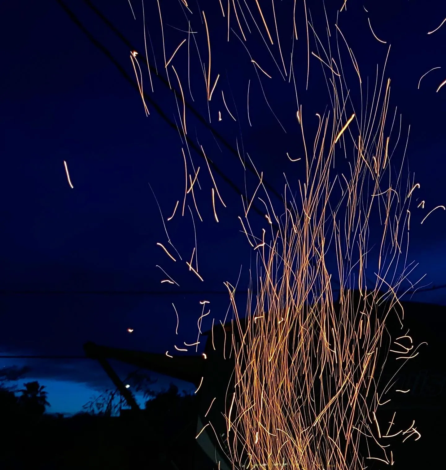 Streaks of bright orange light fall against a deep indigo sky, forming a dense, vertical curtain of glowing lines that scatter upward and outward.