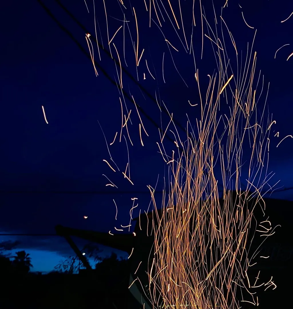 Streaks of bright orange light fall against a deep indigo sky, forming a dense, vertical curtain of glowing lines that scatter upward and outward.