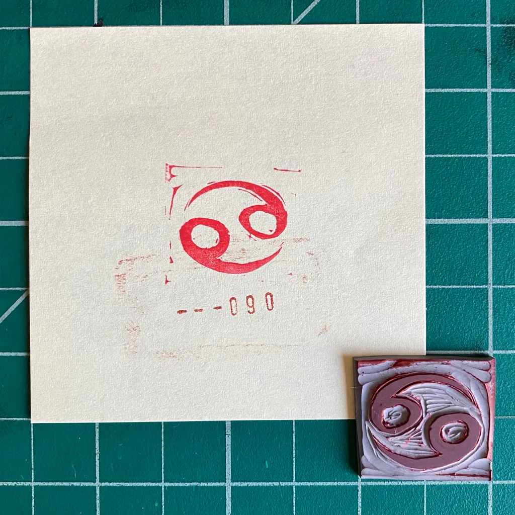 A cream paper on a green grid displays a red circular swirl and the numbers 0-090, positioned above a small square piece featuring layered pink and maroon swirls.