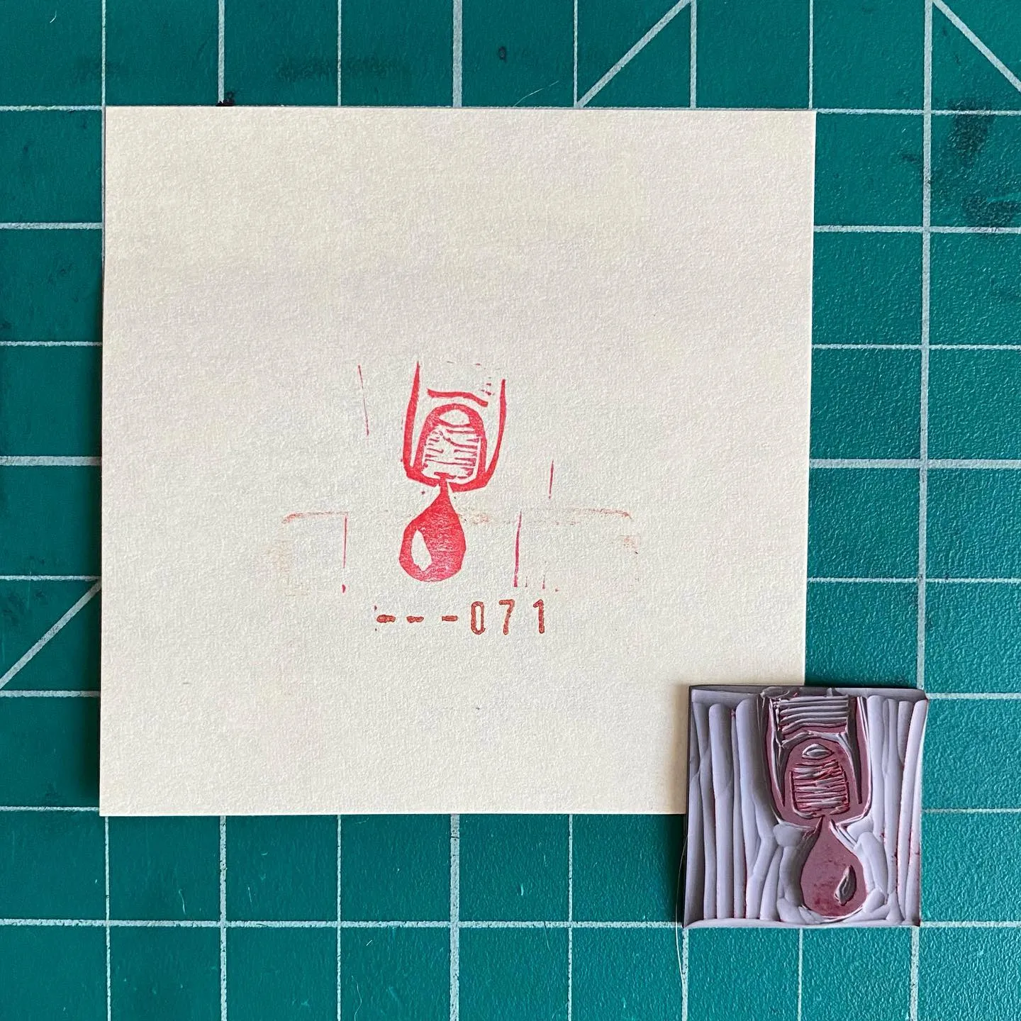 The composition shows a cream paper with a red abstract figure and the numbers --071, placed next to a textured reddish-purple object featuring grooves and a matching teardrop shape.
