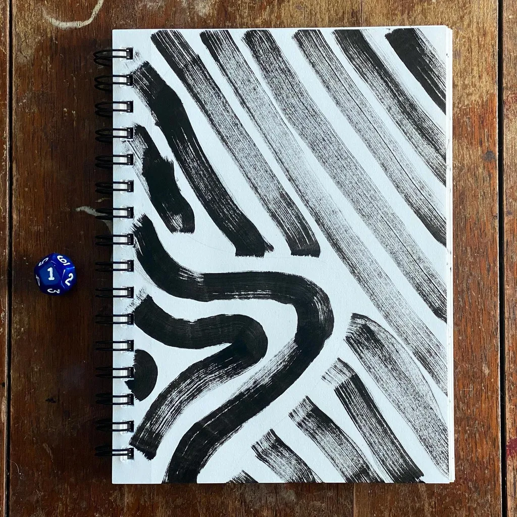 A black and white drawing of thick, gestural stripes and a large curved shape fills an open sketchbook on a wooden surface, next to blue and white dice.