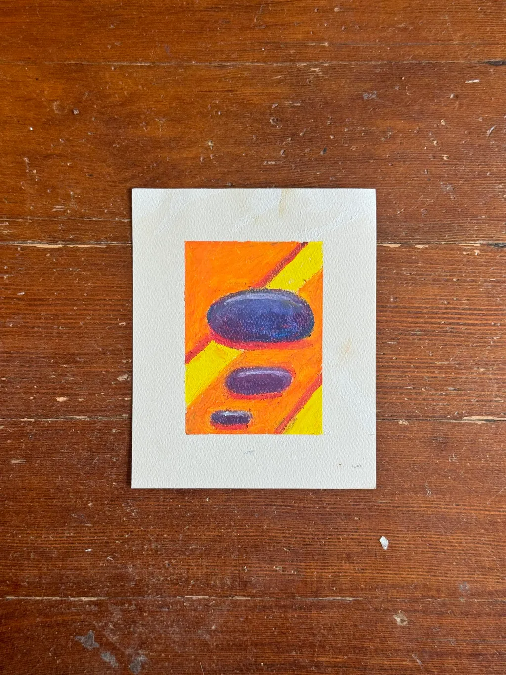 The artwork is centered on a wooden surface, showing vertical bands of orange and yellow intersected by two horizontal ovals: a large dark blue one and a smaller purple one.