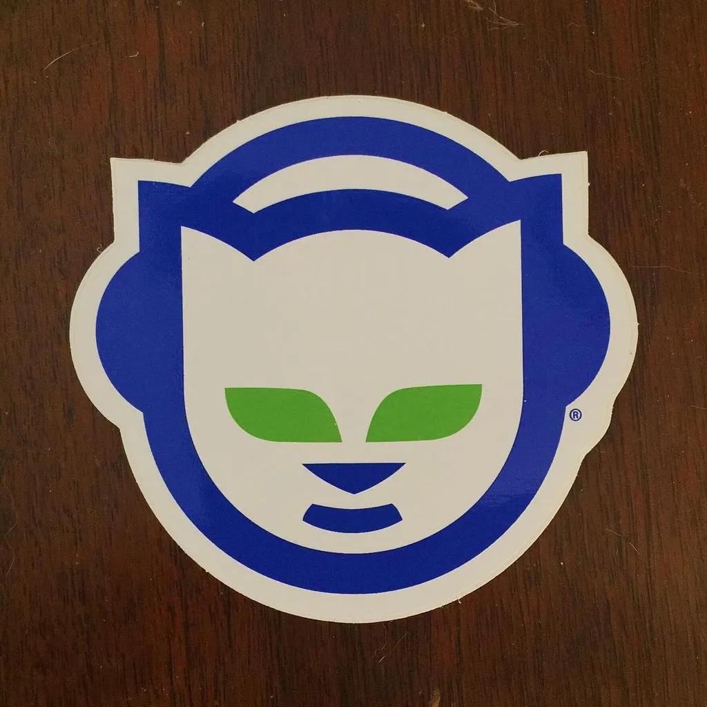 A stylized cartoon mask featuring a white face, blue trim, and large blue ear shapes, with bright green eyes, set against a dark brown wood grain background.